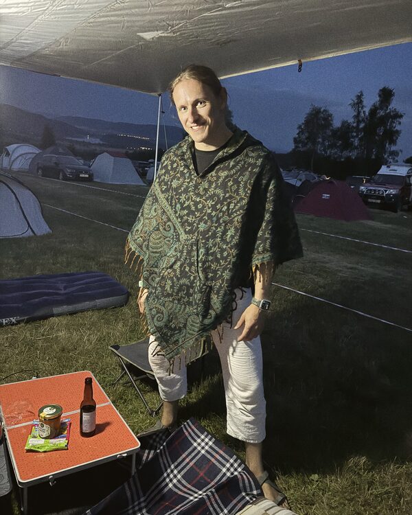 Osoba w ponczo we wzory pod zadaszeniem na polu namiotowym